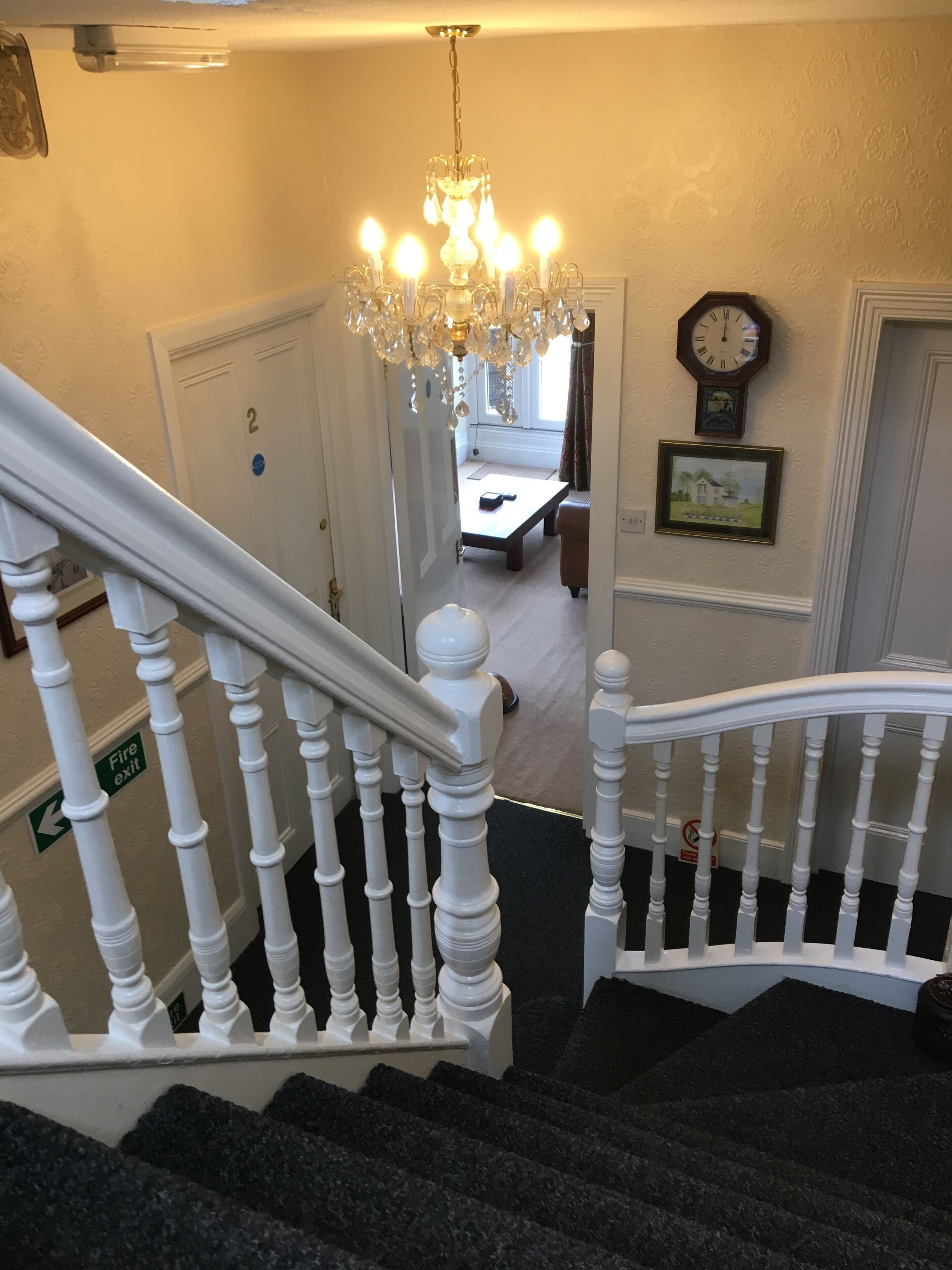 A staircase with white balusters leading to a landing with a chandelier, a clock, and a framed picture on the wall.