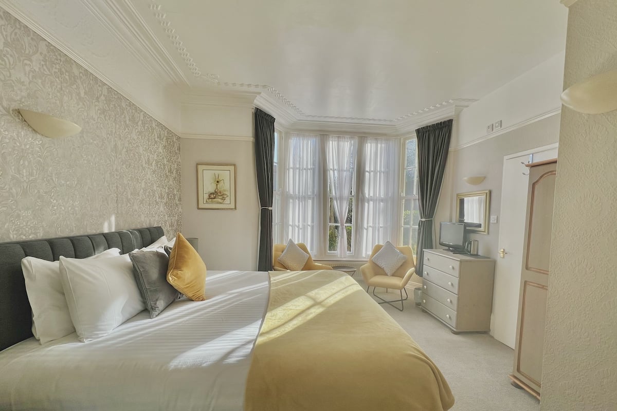 A hotel room with a large bed, a desk with a computer, a chair, and a wardrobe.