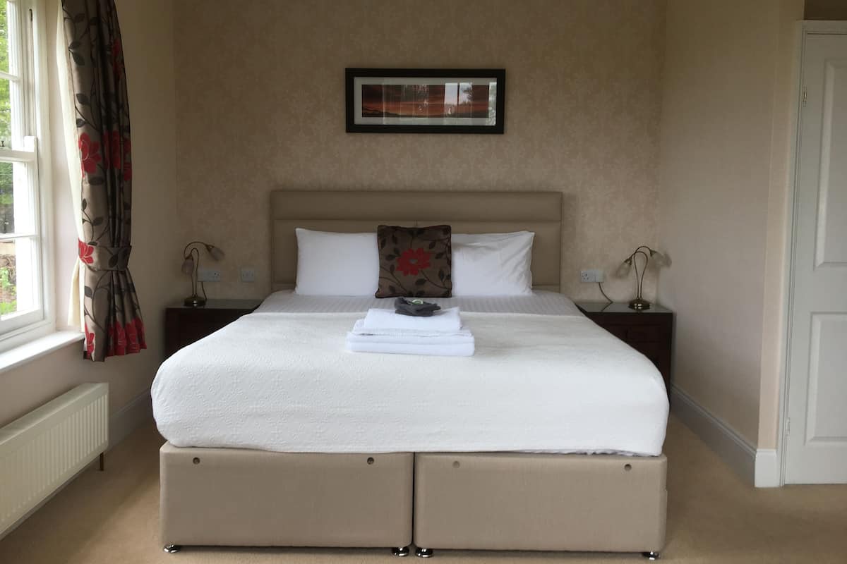 A neatly made bed with a headboard, two bedside tables with lamps, a framed picture on the wall, and a window with curtains.