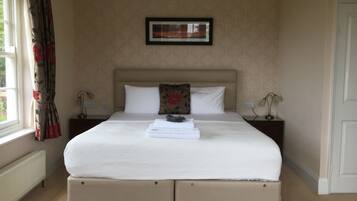 Una cama bien hecha con cabecera, dos mesitas de noche con lámparas, un cuadro enmarcado en la pared y una ventana con cortinas.