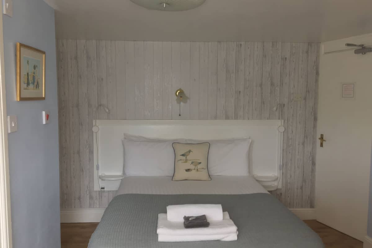 A bedroom with a bed, pillows, a bedside table, and a wall-mounted light fixture.
