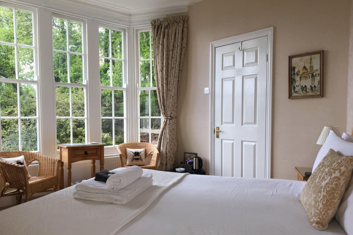 A hotel room with a large bed, a chair, a small table, and a window with curtains.