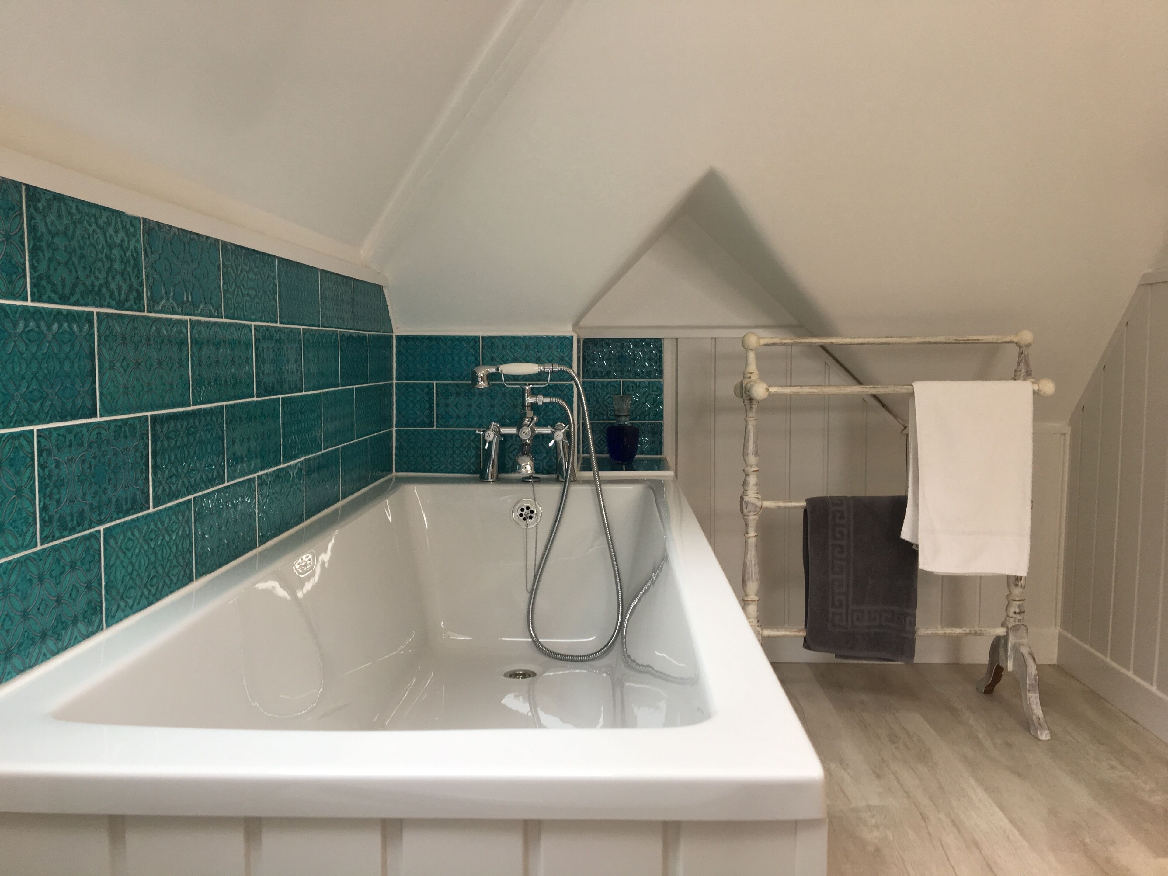 Un baño moderno con una bañera independiente, un perchero y baldosas teal con diseño en las paredes.