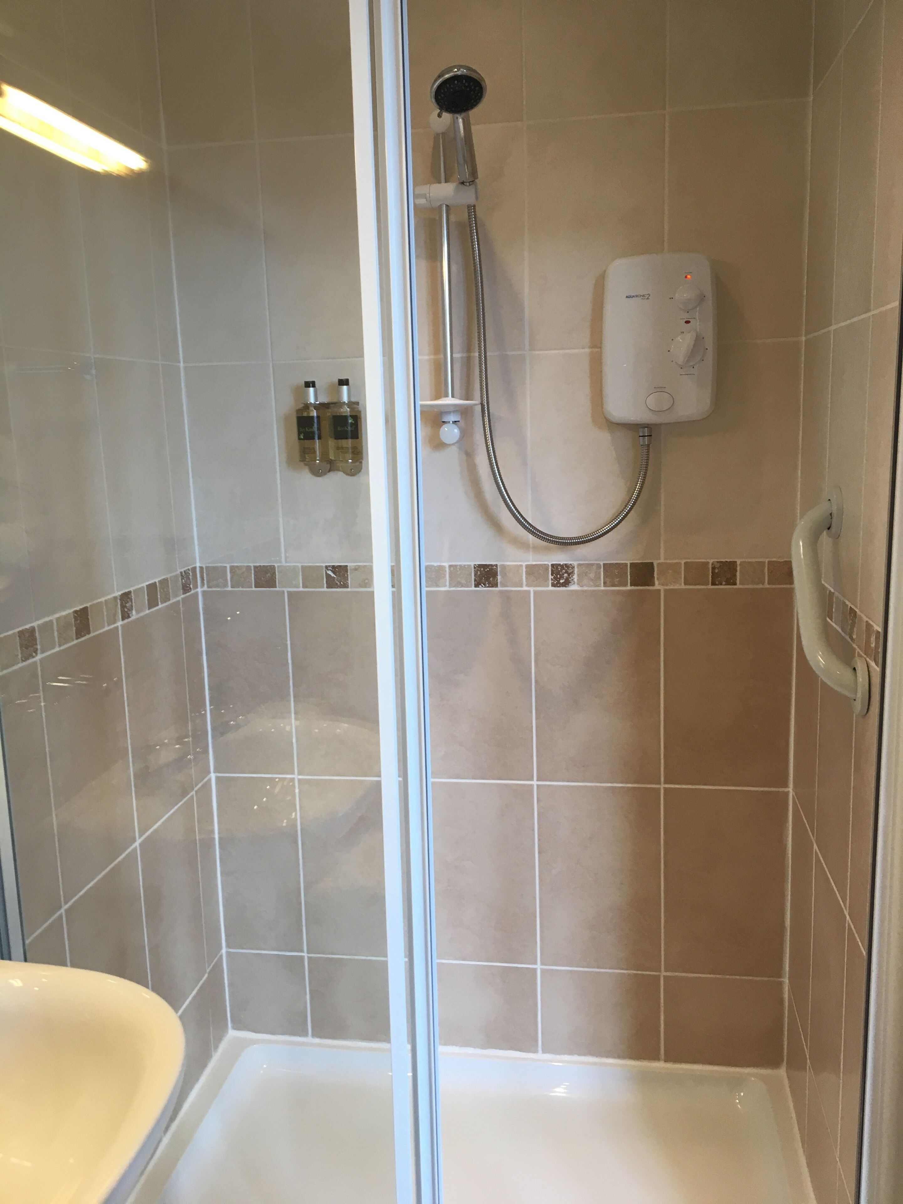Ein Duschbereich mit Glastür, Handbrause, Wandbedieneinheit und Fliesenboden.