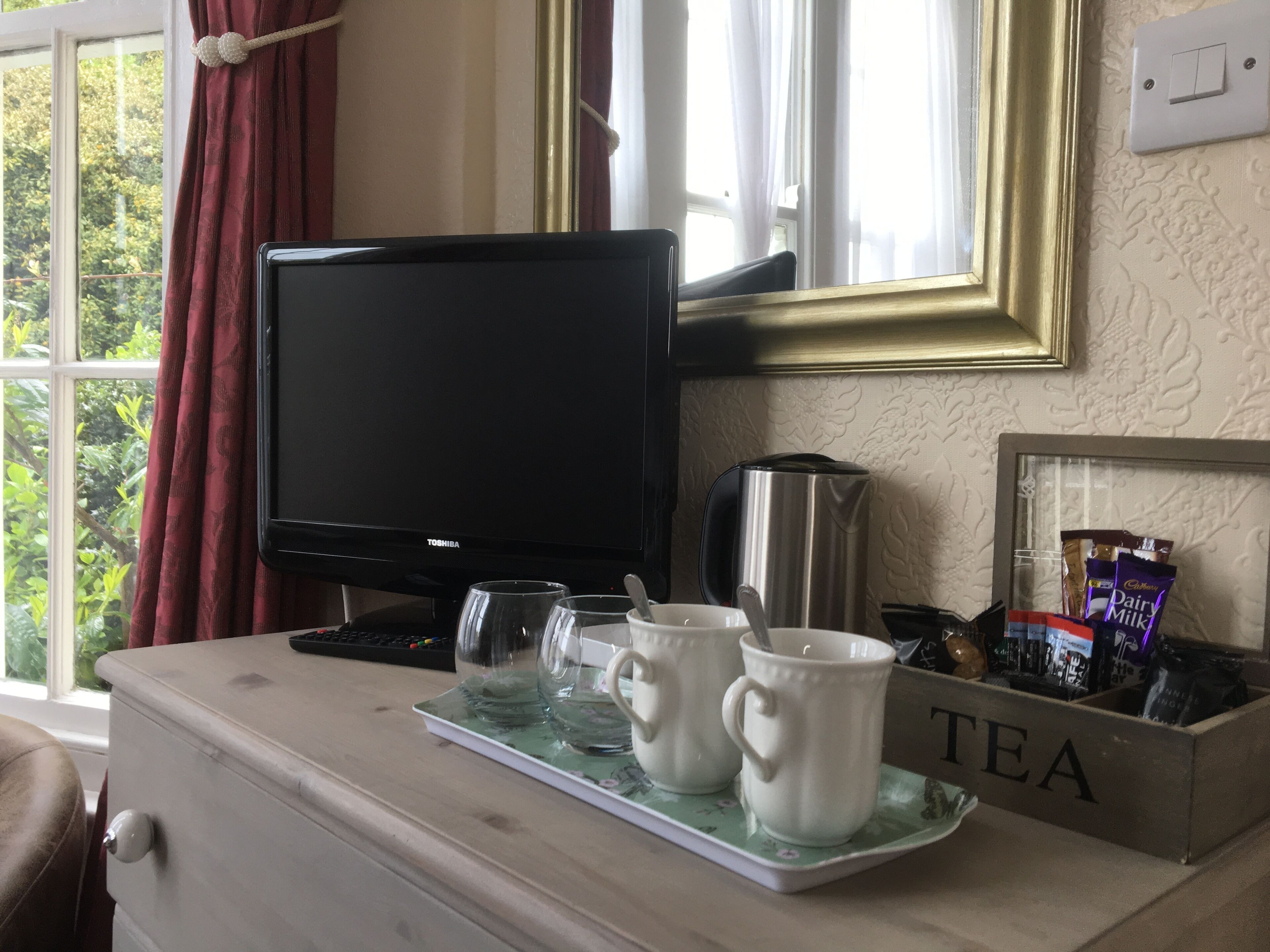 A room with a TV, a coffee maker, two cups, and a tray with a tea sign.
