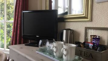 A room with a TV, a coffee maker, two cups, and a tray with a tea sign.