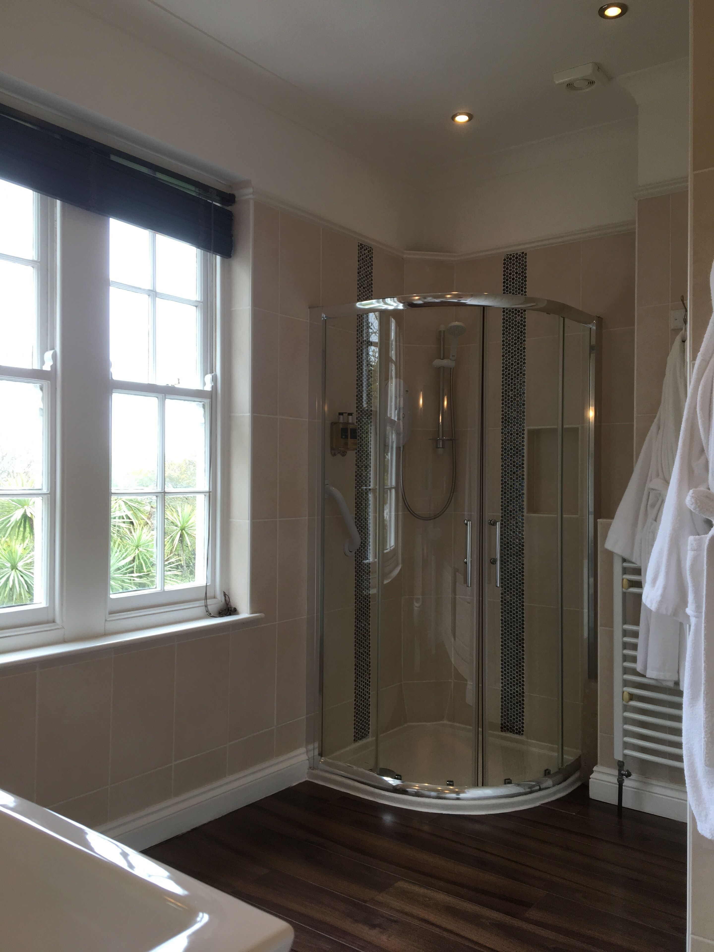 Une douche en verre aux lignes courbes, une baignoire blanche et une fenêtre donnant sur un paysage verdoyant.