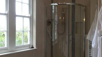 Une douche en verre aux lignes courbes, une baignoire blanche et une fenêtre donnant sur un paysage verdoyant.
