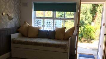 A bedroom with a bed, a sofa bed, a window with a view of greenery, and a door leading outside.