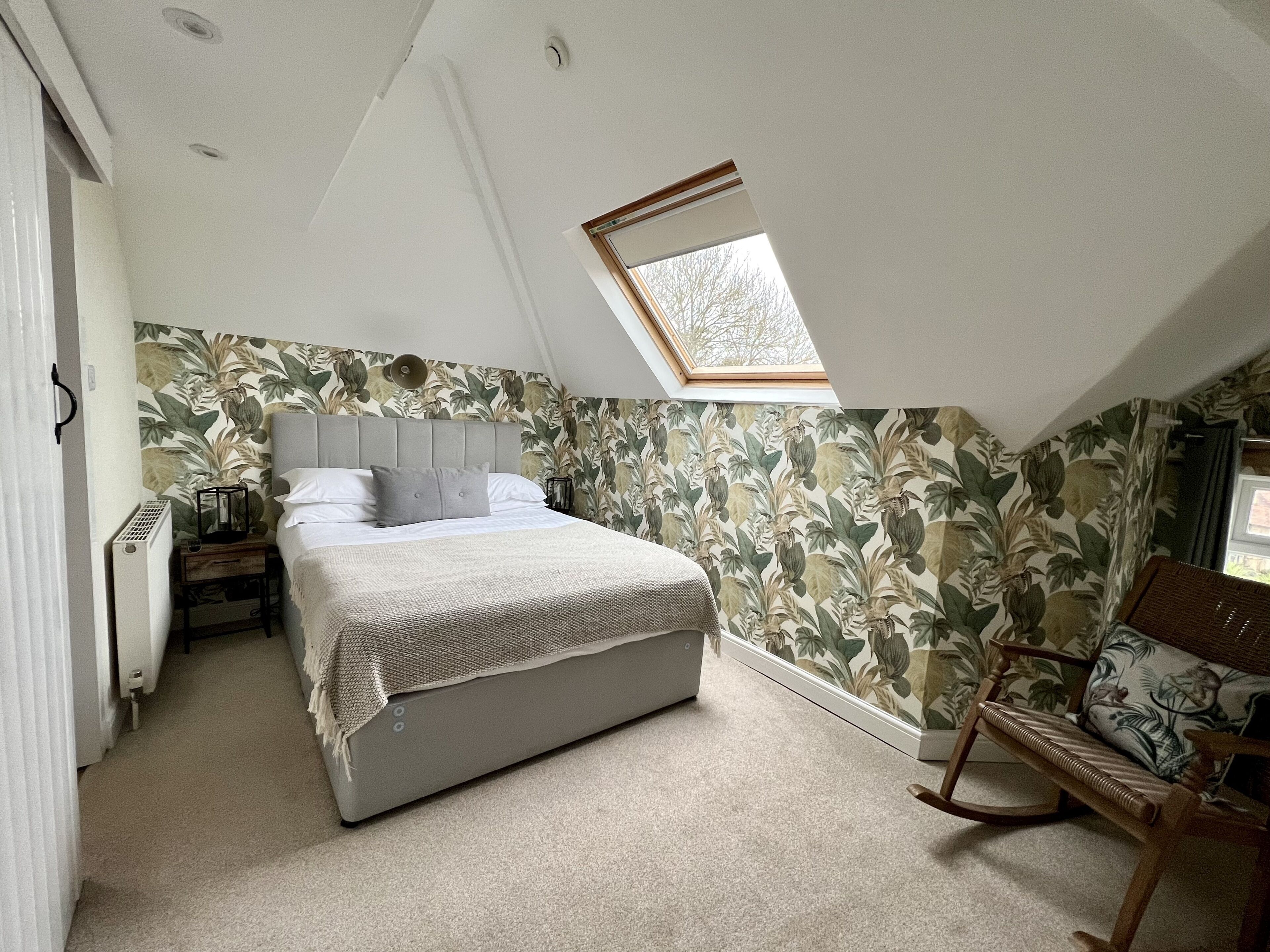 Un dormitorio con una cama, una mesita de noche, un radiador, una ventana y una silla.