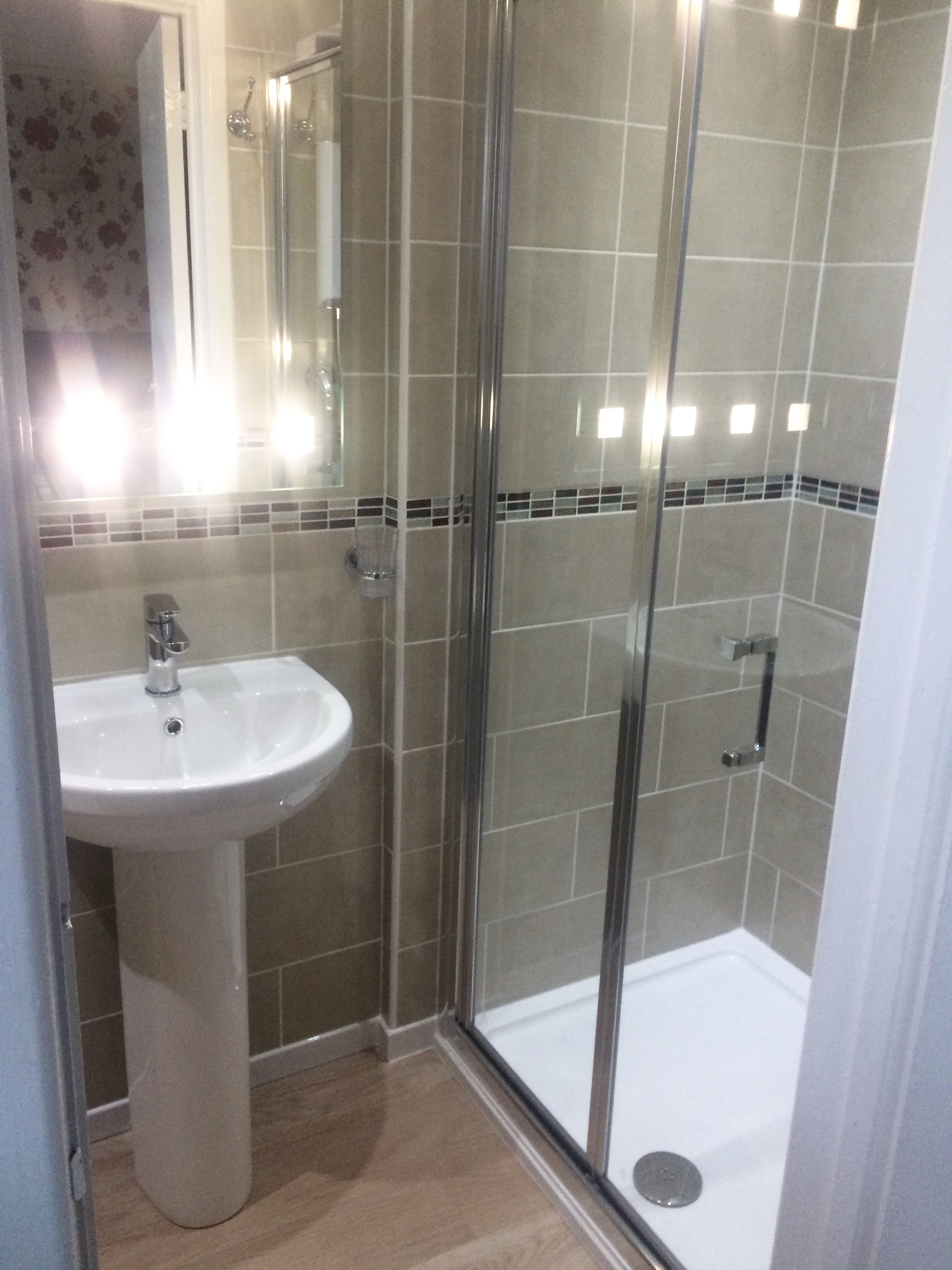 A bathroom with a glass-enclosed shower, a pedestal sink, and tiled walls.
