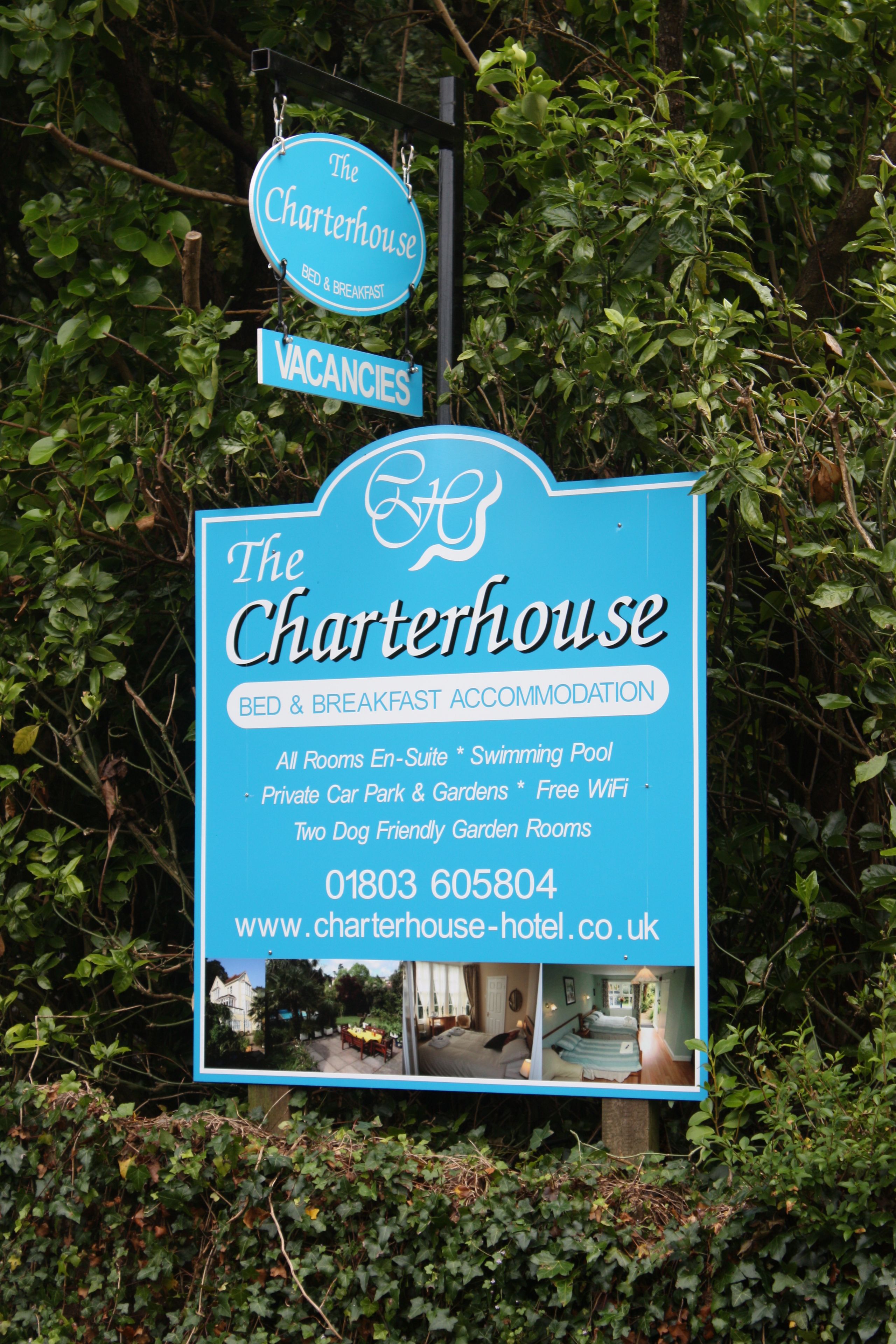 A sign for The Charterhouse, a bed and breakfast accommodation with amenities like a swimming pool, private car park, gardens, free WiFi, and two dog-friendly garden rooms.