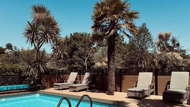 A pool area with lounge chairs and palm trees. - The Charterhouse (Torquay)