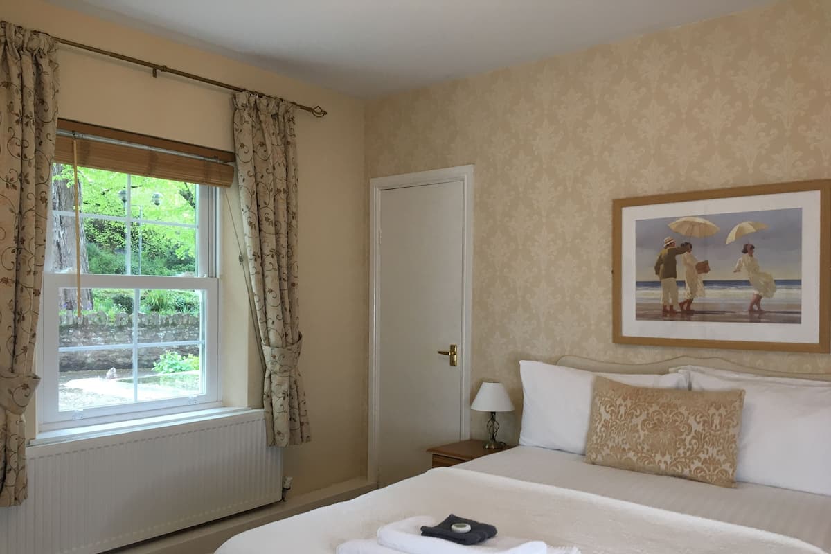 A hotel room with a large bed, a window with curtains, a painting on the wall, and a nightstand with a lamp.