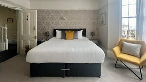 A hotel room with a large bed, a small sofa, a window with curtains, and a door leading to a staircase. - The Charterhouse (Torquay)