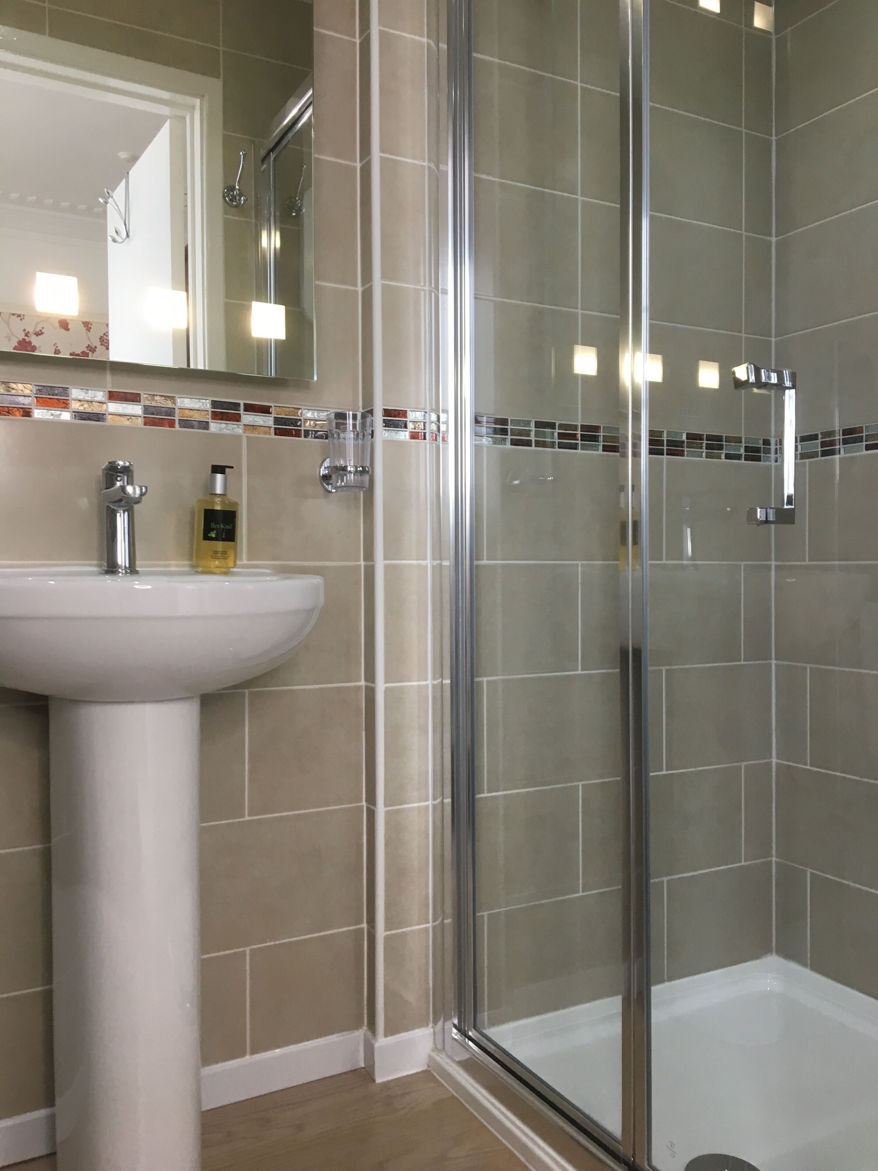 Une salle de bain avec une douche à parois de verre, un lavabo blanc et un miroir au-dessus du lavabo.