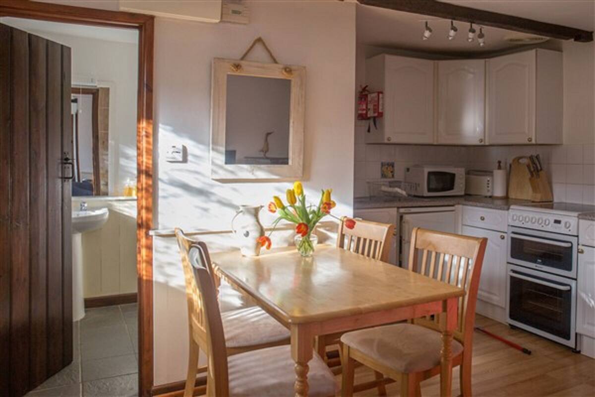Une cuisine avec des meubles blancs, un four à micro-ondes, un four traditionnel et une table à manger avec des chaises.