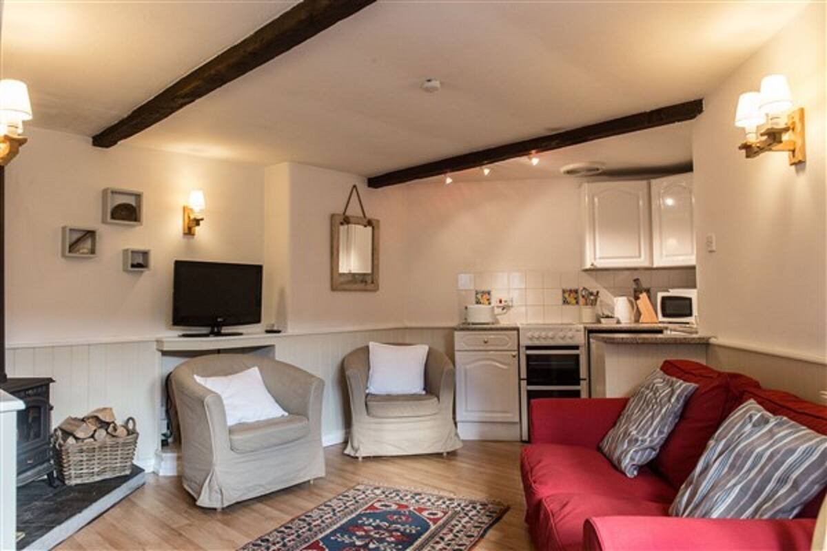 Un salon chaleureux avec une cheminée, deux fauteuils, un canapé rouge et un coin cuisine équipé d’un four à micro-ondes et d’une cuisinière.