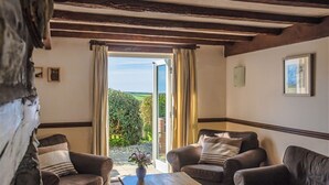A cozy room with a wooden ceiling, two leather sofas, a wooden coffee table, and a view of a garden through an open door. - Cheristow Farm Cottages (Bideford)