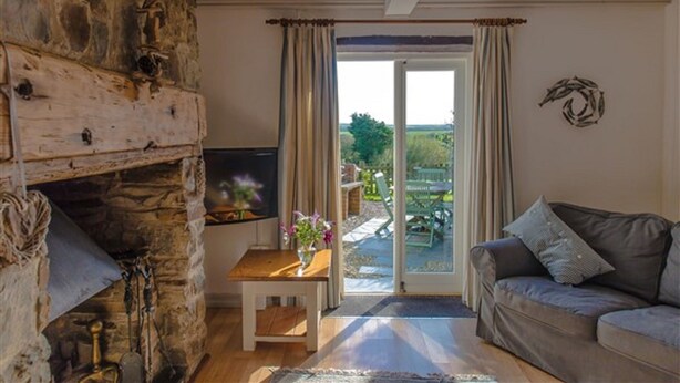 A cozy living room with a stone fireplace, a sofa, and a television. - Cheristow Farm Cottages (Bideford)