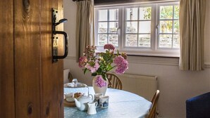 A room with a round table, a vase of flowers, and a window with curtains. - Cheristow Farm Cottages (Bideford)
