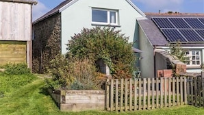 A light blue house with a small window, a wooden fence, and a garden with various plants. - Cheristow Farm Cottages (Bideford)