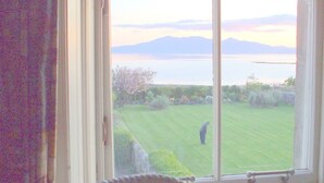 A room with a large window overlooking a well-manicured lawn and a body of water with mountains in the distance.