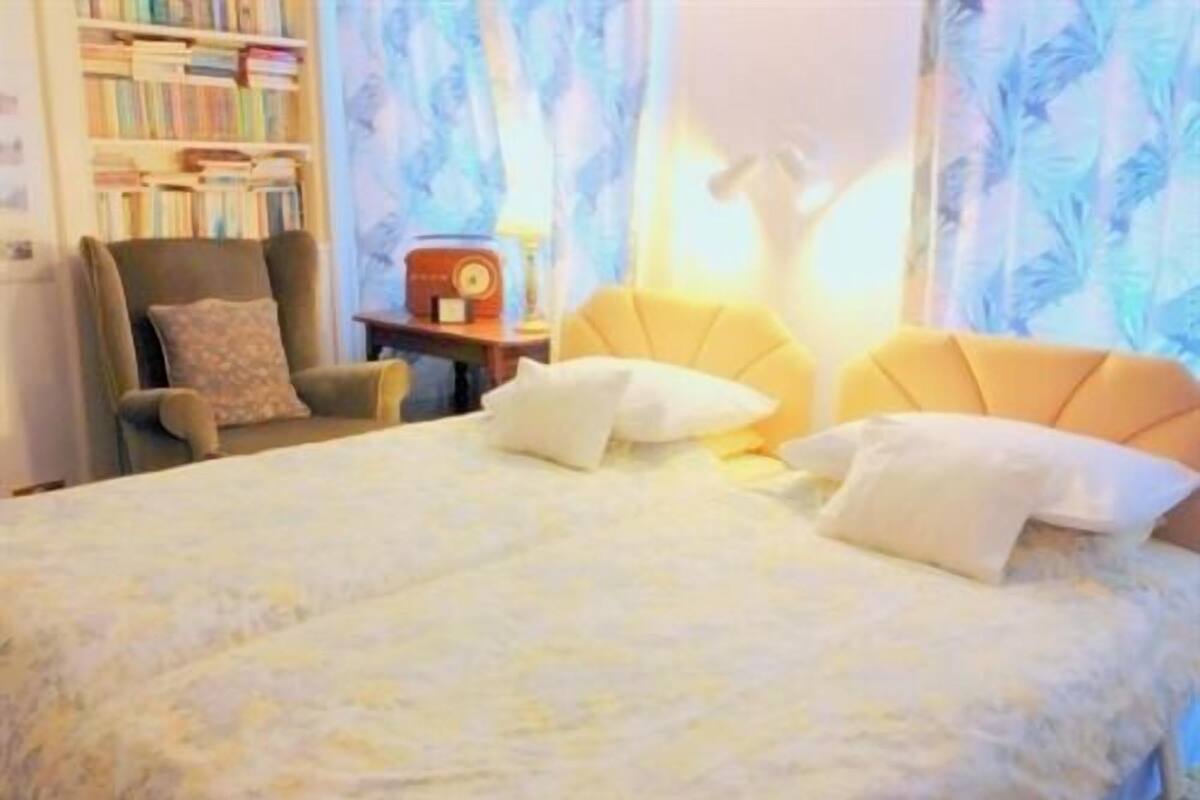 A hotel room with a large bed, a chair, a small table, and a bookshelf.