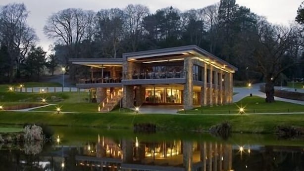 A modern building with a glass facade, a covered outdoor area, and a reflection in the water. - Close House (Newcastle-upon-Tyne)