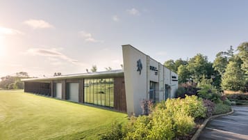 A modern building with a large glass facade, a covered outdoor area, and a well-maintained lawn.
