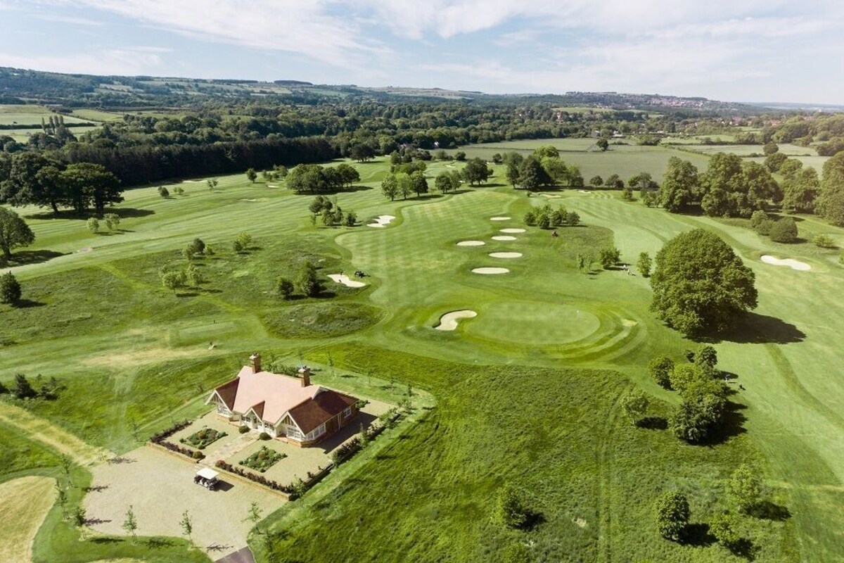 Luftaufnahme eines Golfplatzes mit Clubhaus, Sandbunkern und einer gepflegten Landschaft.