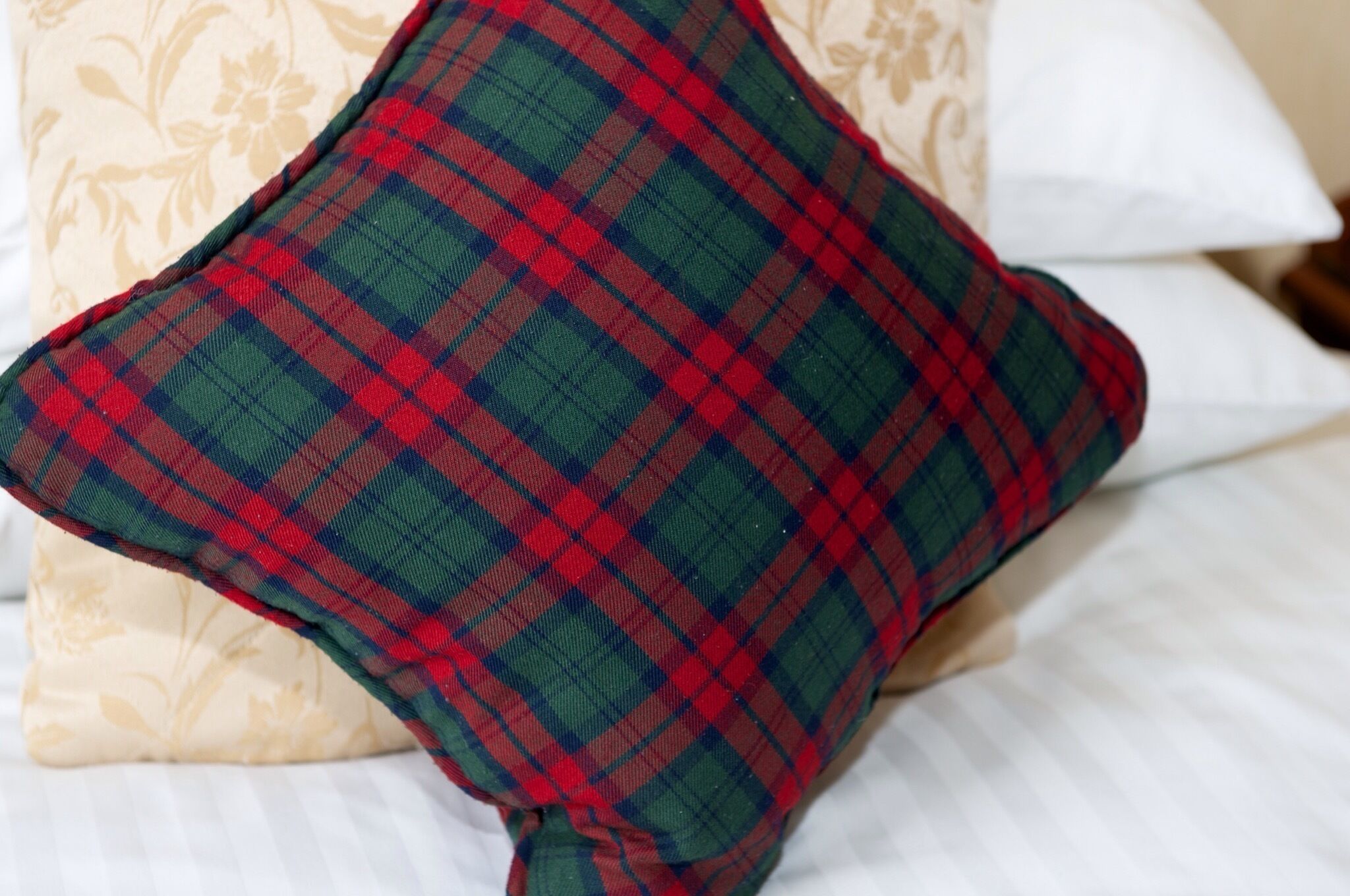 Un cojín escocés sobre una cama, con un cojín de estampado floral detrás.