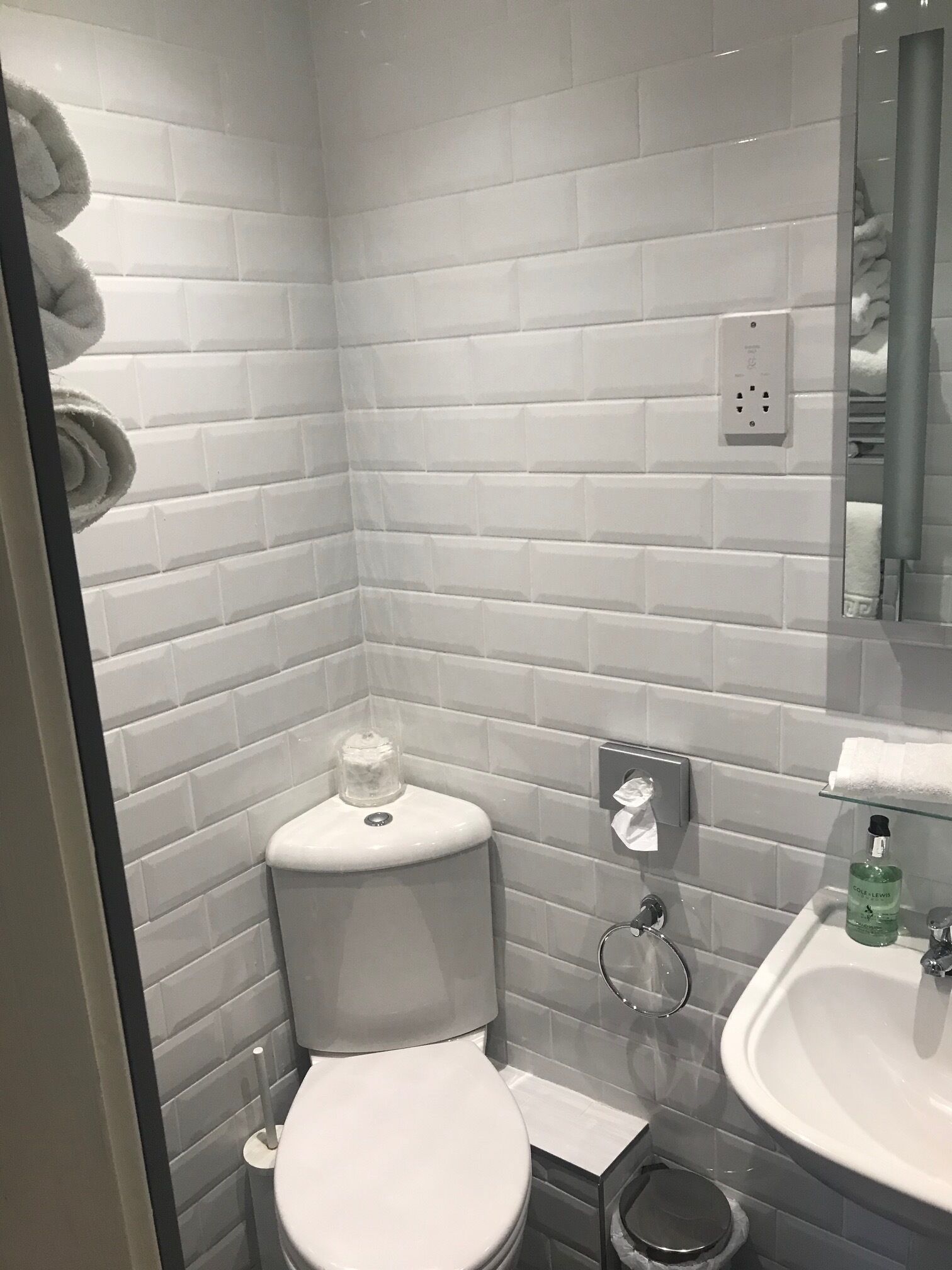 Un baño moderno con azulejos blancos tipo metro, un inodoro, un lavabo y una ducha con mampara de vidrio.