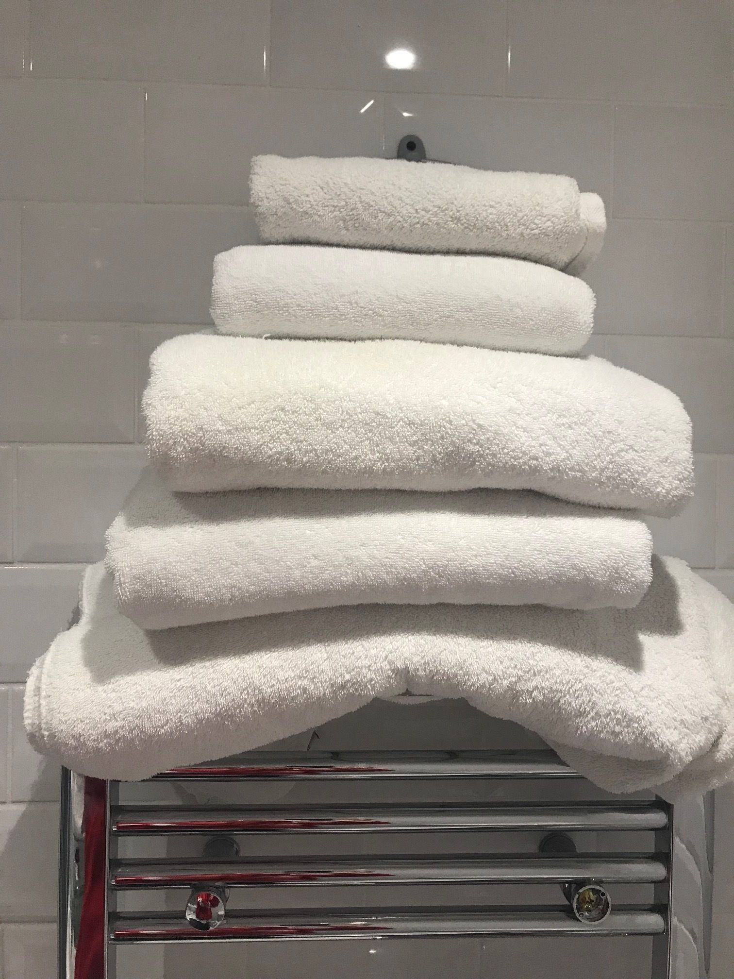 A stack of white towels on a metal rack in a bathroom with white tiles.