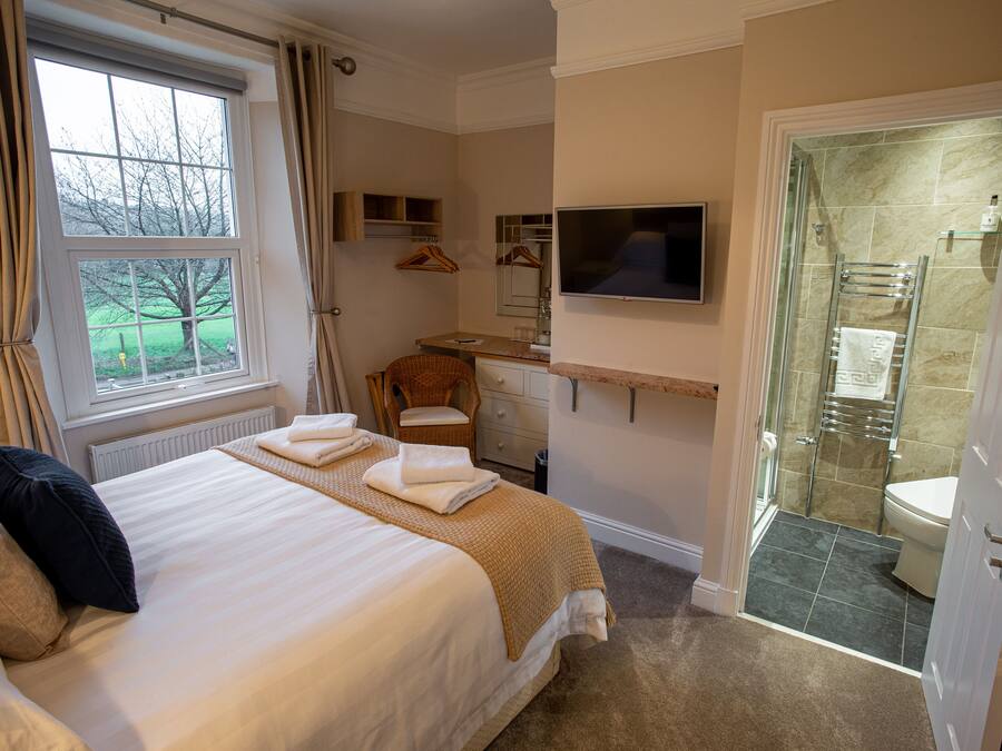 Habitación de hotel con una cama grande, televisión, ducha y vistas al exterior.