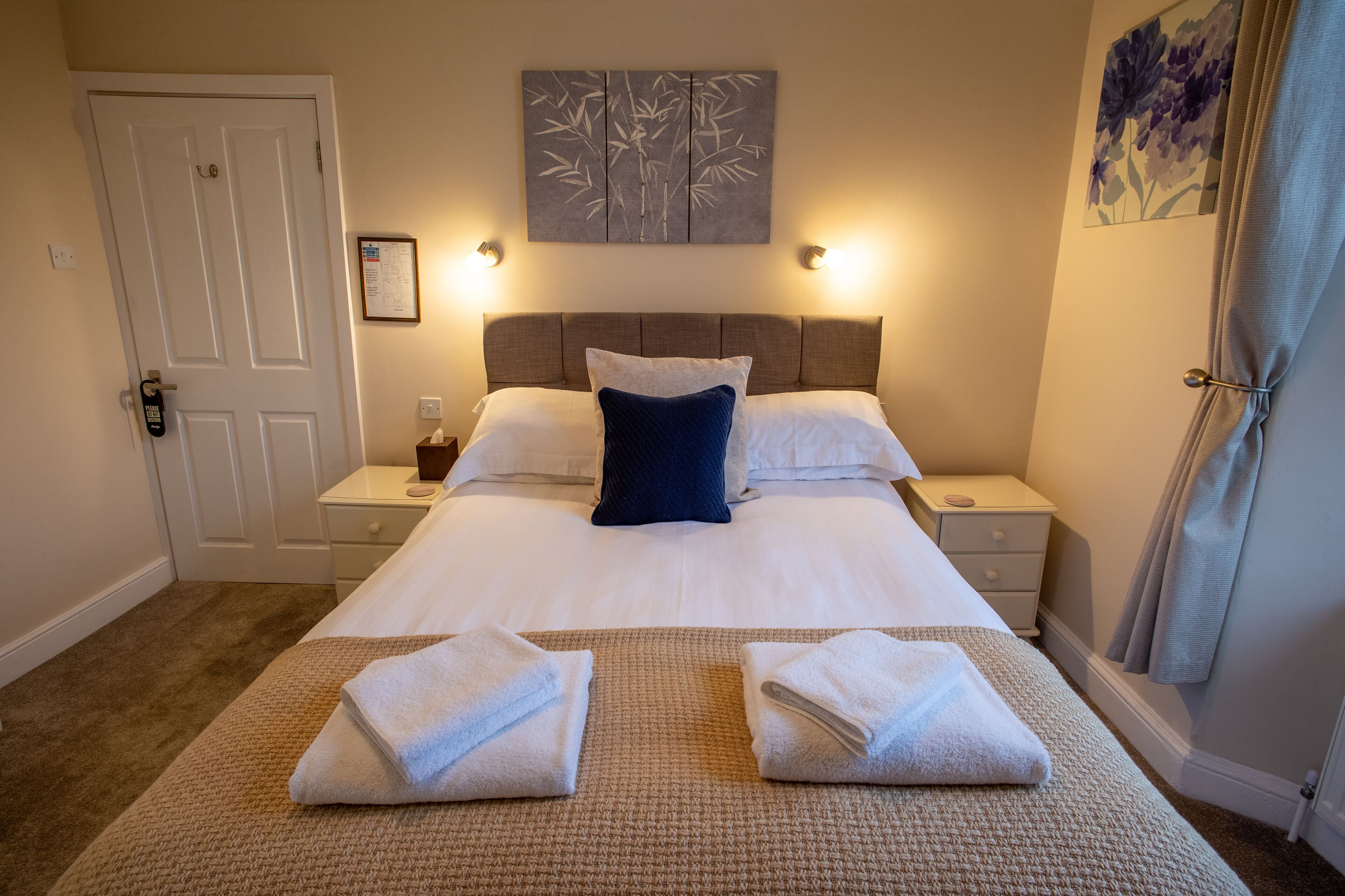 A hotel room with a large bed, two bedside tables, a wall-mounted artwork, and a door.