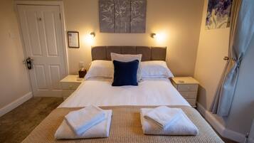 A hotel room with a large bed, two bedside tables, a wall-mounted artwork, and a door.