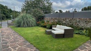 A patio area with a stone pathway, a grassy lawn, and a wicker sofa with cushions. - Deanfield Bed and Breakfast (Lydney)