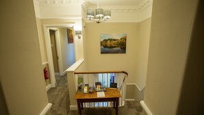 A hallway with a wooden table, a painting, and a chandelier. - Deanfield Bed and Breakfast (Lydney)