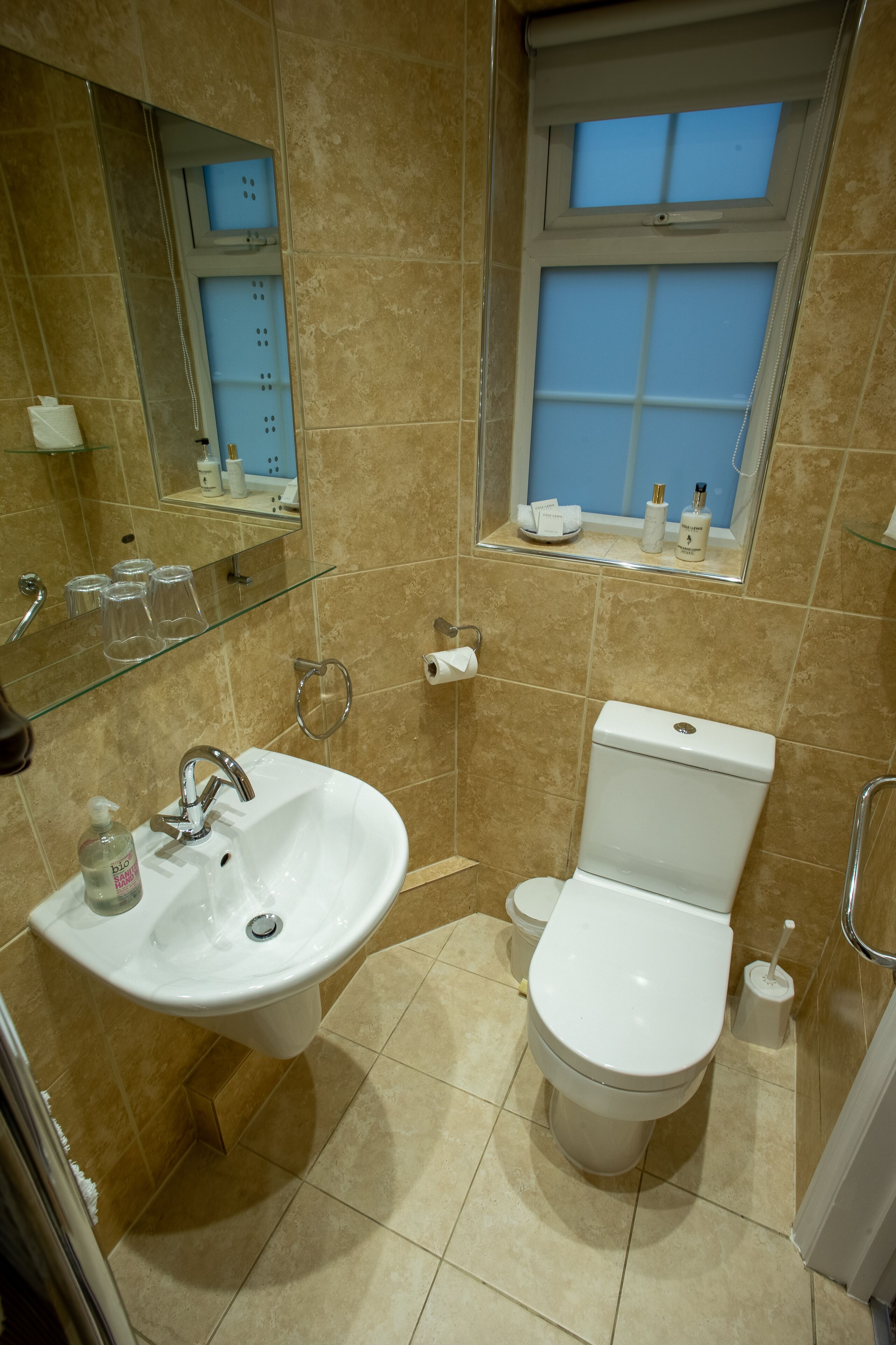 Un baño con lavamanos, inodoro y ventana sobre el inodoro.