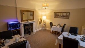 A dining area with two tables, chairs, a fireplace, a mirror, and a wall-mounted painting. - Deanfield Bed and Breakfast (Lydney)
