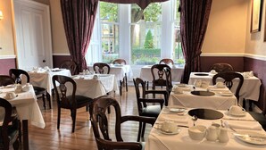 A dining area with multiple tables set for service, wooden chairs, and a view of the outside through large windows. - Glenalmond Guest House (Edinburgh)