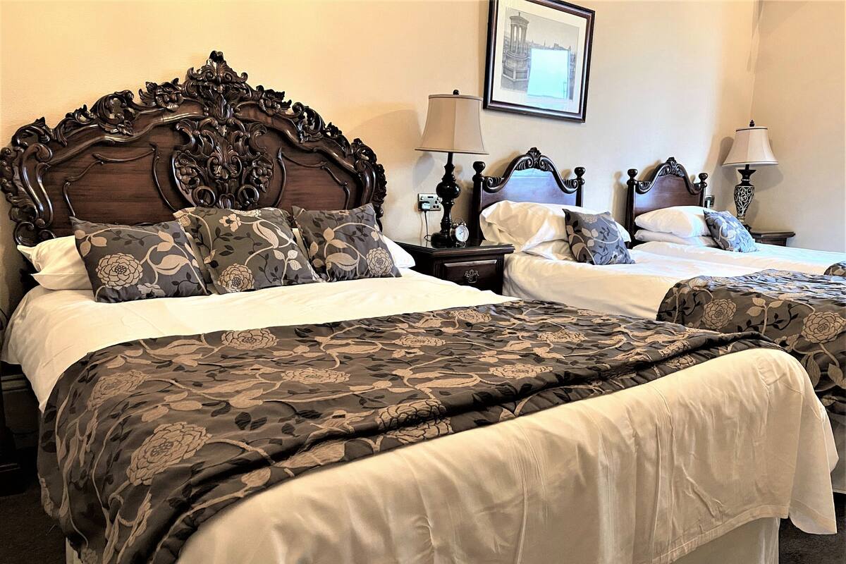 A hotel room with two beds, ornate headboards, floral-patterned bedding, and bedside lamps.
