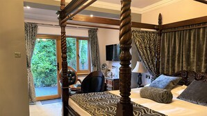 A four-poster bed with a patterned bedspread, a bedside table with a lamp, and a view of greenery through the window. - Glenalmond Guest House (Edinburgh)
