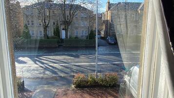 Une vue à travers une fenêtre donnant sur une rue, avec un bâtiment en arrière-plan, un lampadaire et une voiture garée.