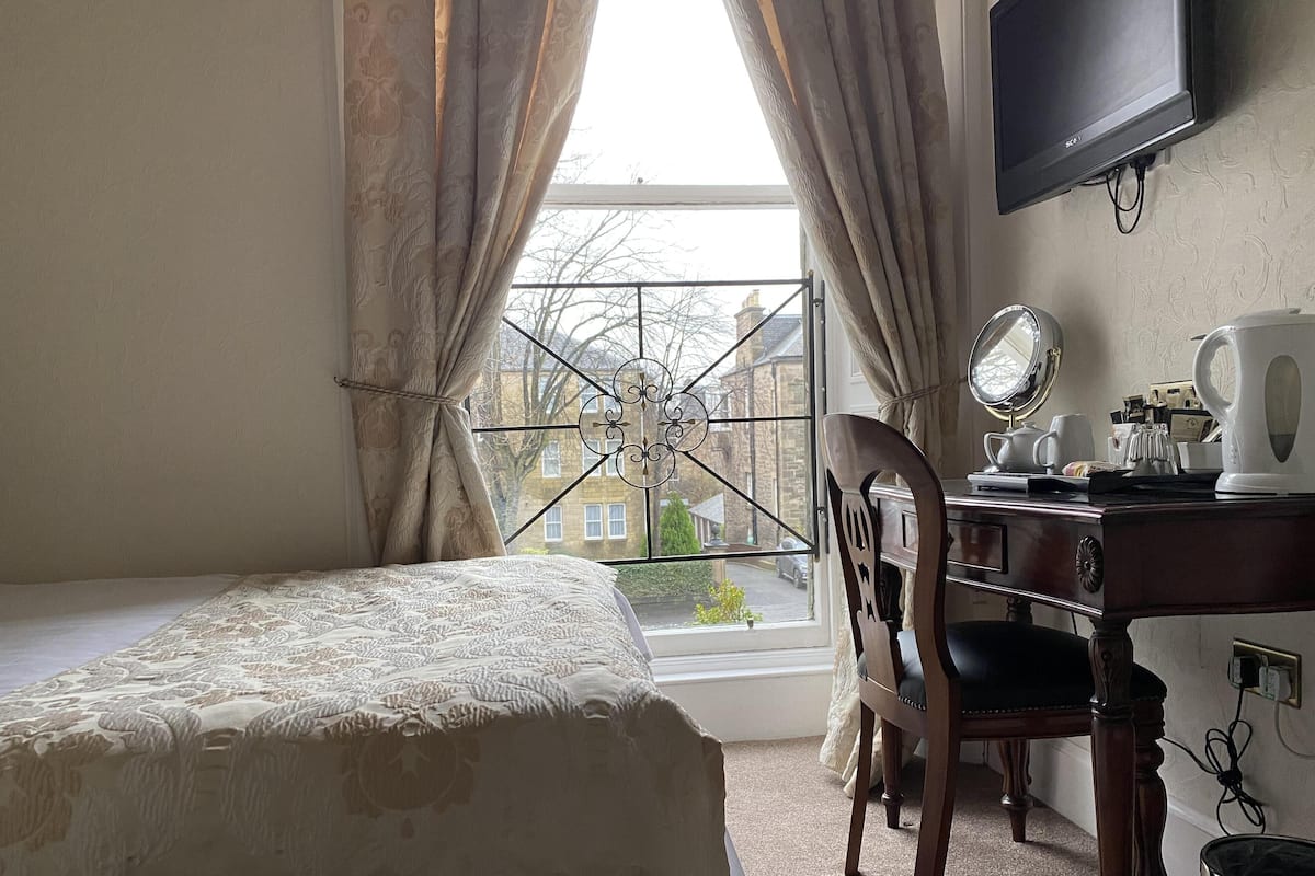 A bedroom with a bed, a desk with a chair, a television, and a window with curtains.