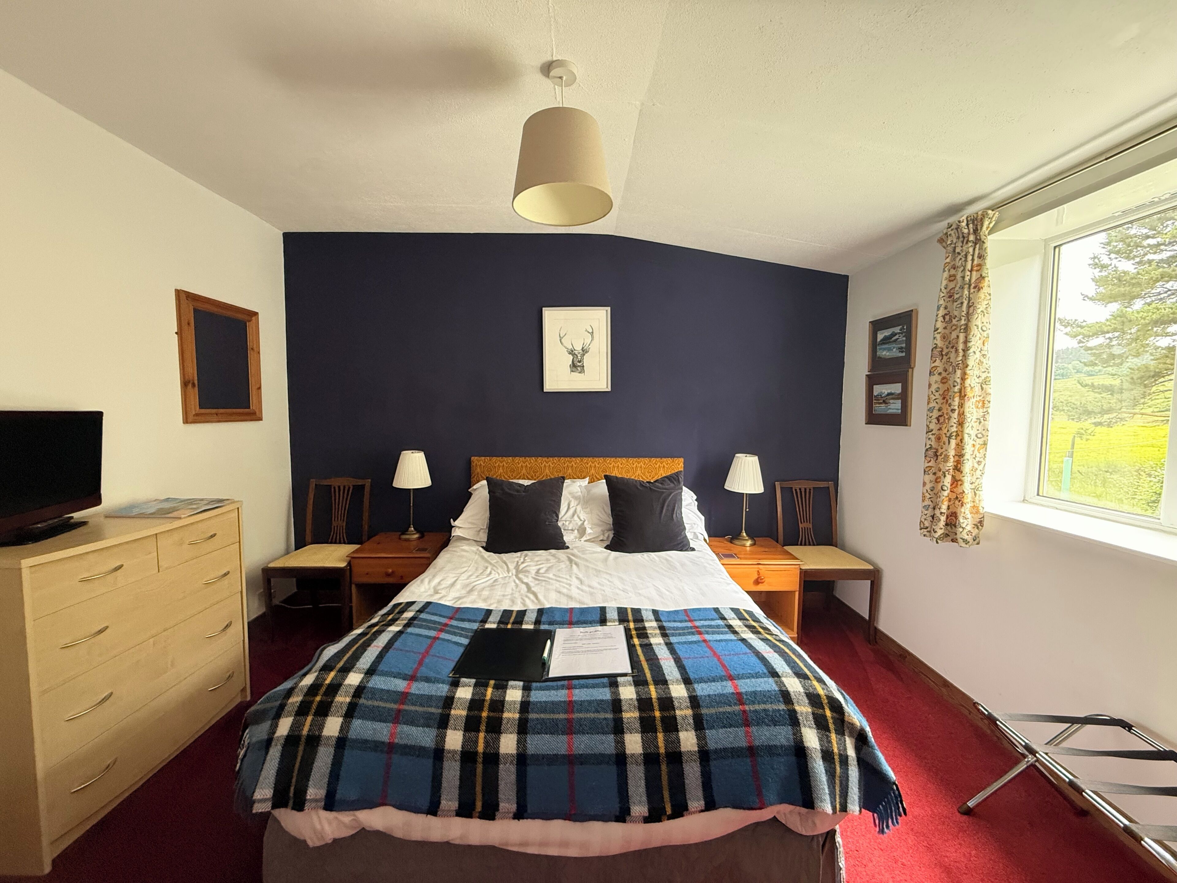 A hotel room with a bed, two bedside tables, a television, a dresser, and a window with curtains.