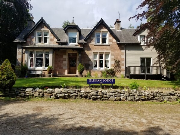 Une maison à deux étages avec une façade en pierre, un porche à l’avant et une enseigne indiquant « Glenan Lodge ».