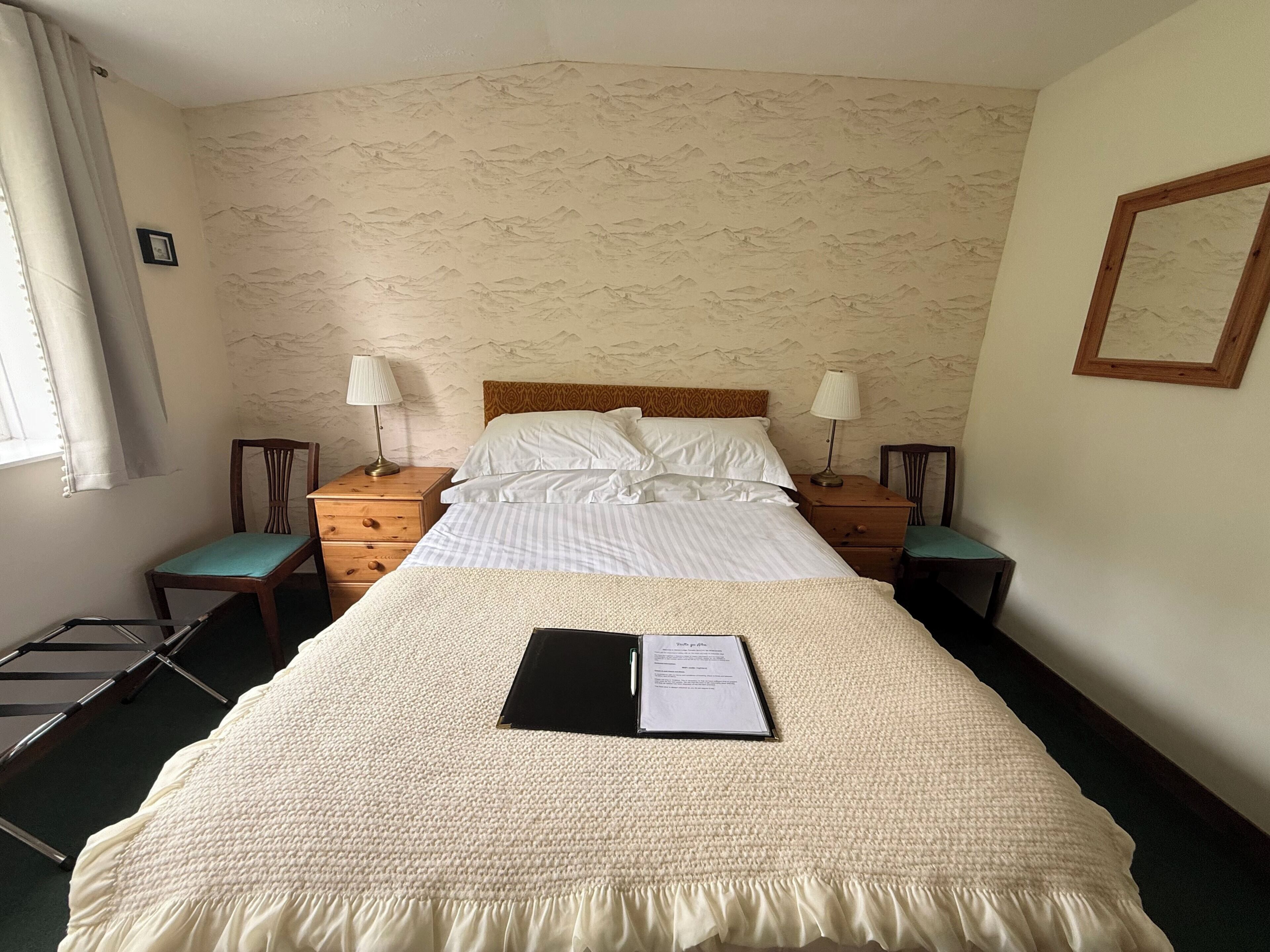 Un letto matrimoniale con una coperta a trama decorativa, due comodini con lampade, una testiera in legno e una parete con motivo montano.