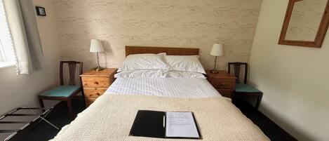 Un letto matrimoniale con una coperta a trama decorativa, due comodini con lampade, una testiera in legno e una parete con motivo montano.